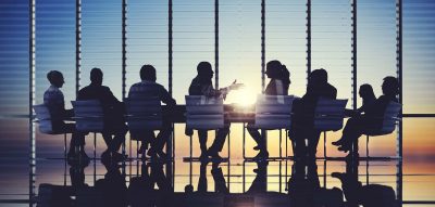 A group of people at a table in a large conference room with the sun coming up in the distance